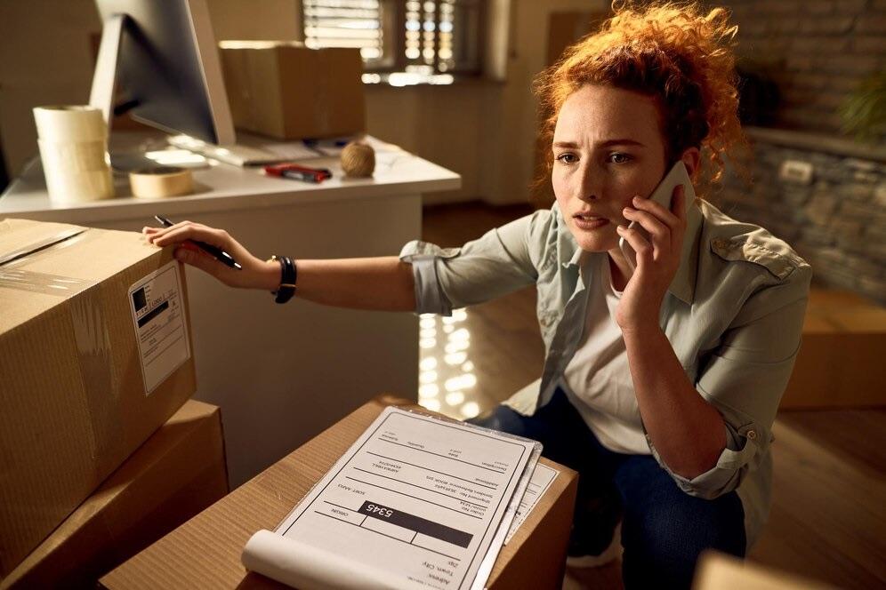 Worried woman on a phone call next to an opened delivery box and its paperwork